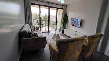En moderne stue med sofa, lænestole, sofabord og fjernsyn på væggen.