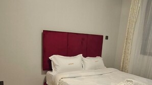 Ein ordentlich bezogenes Bett mit weißen Leinen und einem roten Kopfteil in einem Zimmer mit einem gemusterten Teppich.