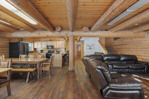 A log cabin interior with a dining area, kitchen, and a leather sofa. - River Lodge | River Facing, Yellowstone, & Pets! (Island Park)