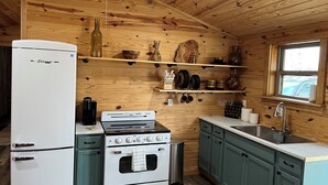 Una cocina compacta con paredes de madera, un refrigerador blanco, una estufa y un lavamanos.