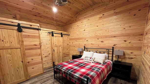 Un dormitorio de cabaña acogedor de madera, con una cama, dos mesitas de noche y un ventilador de techo.