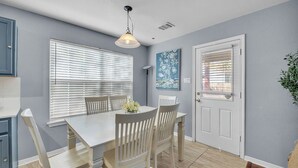 Uma área de refeições com uma mesa e cadeiras brancas, um lustre pendurado e uma porta com janela.