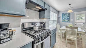 A modern kitchen with a gas stove, a kettle, and a coffee maker. There is a dining area with a table and chairs. - Cozy 3BR Duplex in Prime Austin | Near Downtown (Austin)