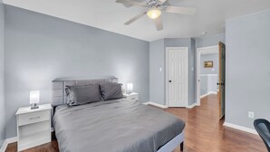 Quarto com cama, mesas de cabeceira, ventilador de teto e porta para outro cômodo.