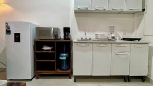 Une cuisine compacte avec des meubles blancs, un four à micro-ondes, une machine à café et un distributeur d’eau.