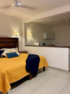 Ein Hotelzimmer mit Bett, Nachttischlampen, Deckenventilator und einer Küchenzeile mit Kühlschrank und Spüle.