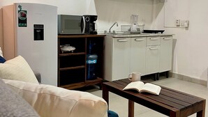 Un espace de vie compact comprenant un coin cuisine, un canapé, une table basse et un distributeur d’eau.