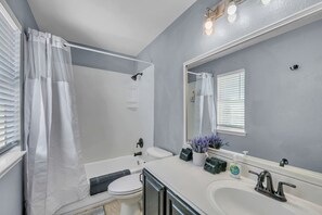 Ein Badezimmer mit Badewanne, Toilette und Waschbecken. Über dem Waschbecken befindet sich ein großer Spiegel und ein Duschvorhang.