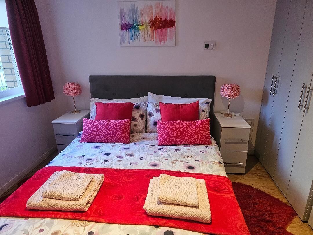 A bedroom with a bed, two nightstands, a wardrobe, and a window with curtains.