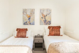 A hotel room with two beds, a nightstand, and two wall-mounted paintings of deer.