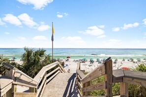 Une promenade en bois menant à une plage où se trouvent des parasols et des gens.