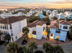 Un quartier résidentiel en bord de mer, avec des maisons blanches et bleues, dont certaines sont dotées de balcons, et des palmiers.