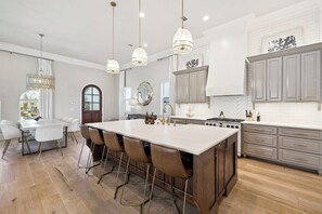Une cuisine spacieuse dotée d’un grand îlot central, de luminaires suspendus et offrant une vue sur l’extérieur.