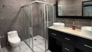 Moderni kylpyhuone, jossa on lasiseinällä varustettu suihku, wc ja pesuallas, jossa on peili ja allas.