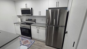 A modern kitchen with white cabinets, stainless steel appliances, and a patterned rug.
