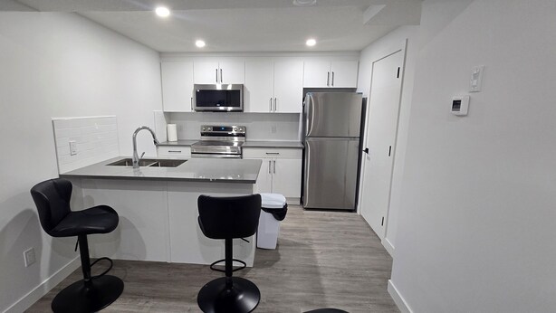 A modern kitchen with white cabinets, stainless steel appliances, and two black bar stools.