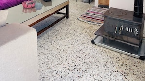 Un espacio habitable compacto con sofá, una mesita de centro de vidrio, una zona de cocina con estufa, dispensador de agua y un refrigerador pequeño.
