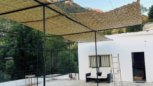 Un patio con suelo de piedra, un edificio blanco, una escalera y una zona de estar cubierta.