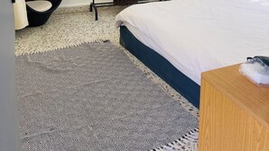 Un dormitorio con cama, una silla colgante, una ventana con persianas, un estante en la pared y una pequeña cesta.
