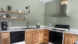 A compact kitchen with wooden cabinets, a gas stove, a dishwasher, and a coffee maker. - Cozy 2-bedroom cottage in historic Calumet (calumet)