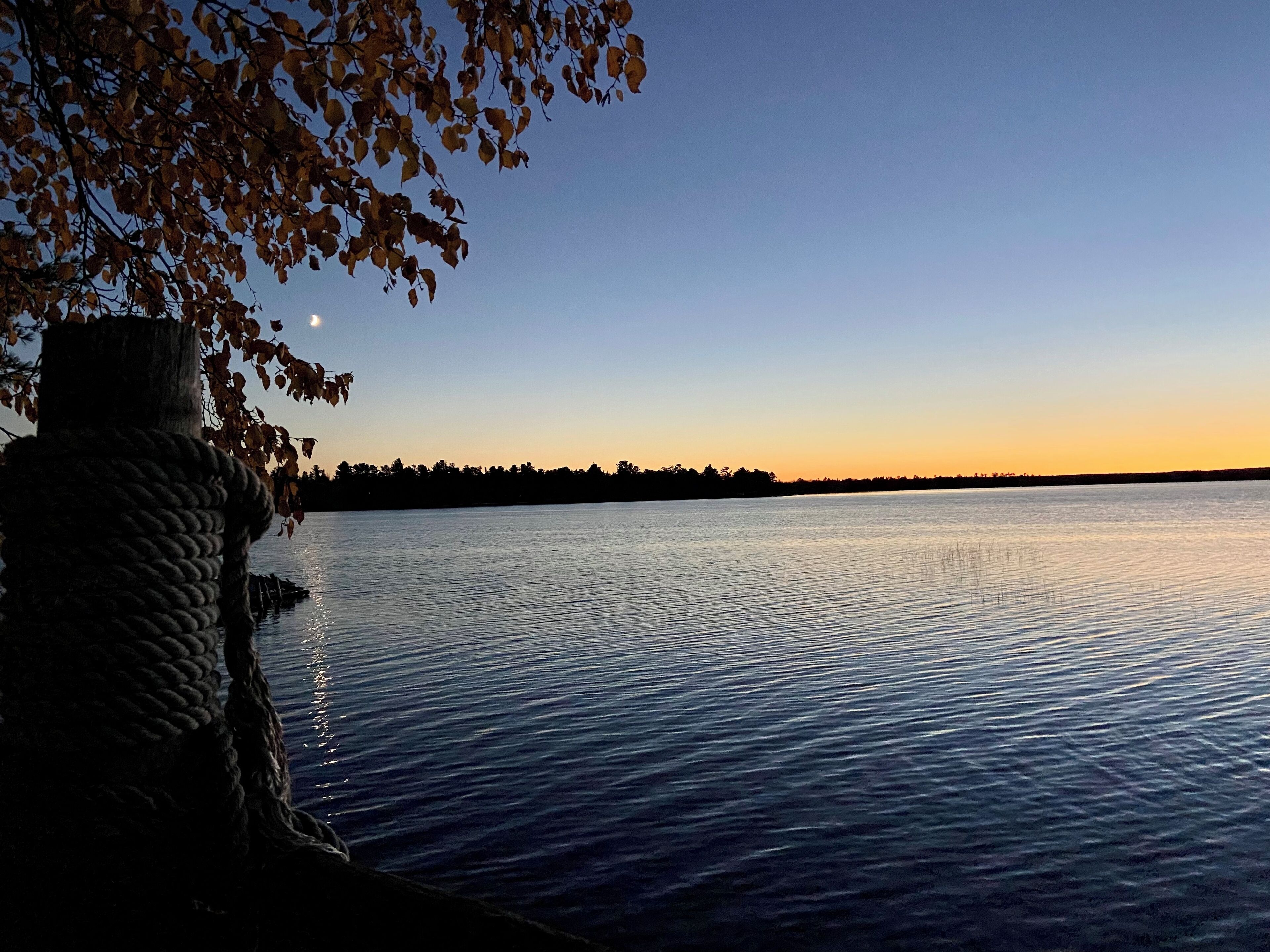 Un lac paisible au coucher du soleil, avec une structure en pierre sur la gauche et une branche d’arbre au-dessus.