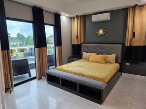 A modern bedroom with a large bed, a bench, a nightstand, and a view of the outside balcony.