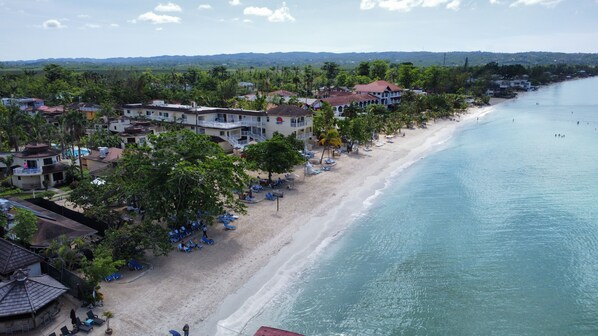 A coastal hotel with multiple buildings, a sandy beach, and a clear view of the ocean.