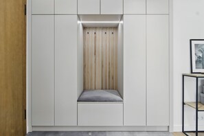 A modern wardrobe with a built-in bench, a wooden slat panel, and a grey cushioned seat. - Luxury 2-room apartment in Praga-Północ Port Praski (Warszawa)