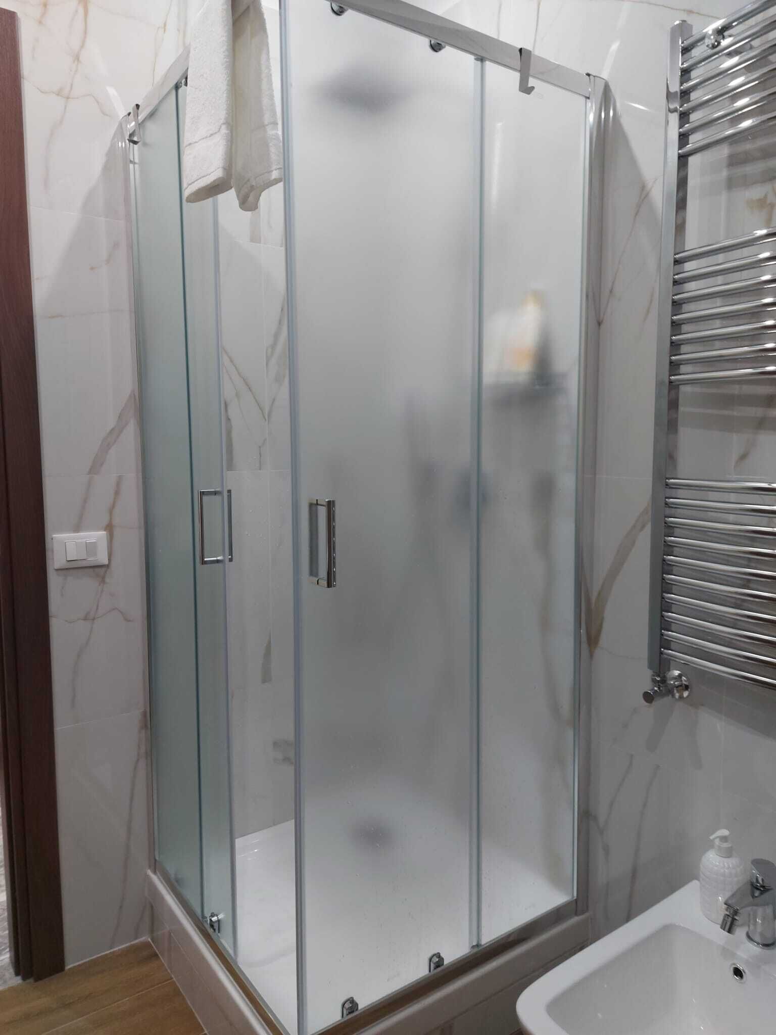 A glass-enclosed shower with a chrome frame, a white sink, and a chrome towel rack.