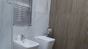 A modern bathroom with a bidet, a toilet, a glass shower enclosure, and a wooden panel wall. - Arte Mia suite (Reggio Calabria)
