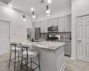 A modern kitchen with a central island, bar stools, stainless steel appliances, and pendant lighting. - Luxurious Apartment in Houston. (Houston)