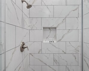 A shower area with white marble tiles and a built-in shelf with toiletries. - Luxurious Apartment in Houston. (Houston)