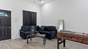 Ein Wohnzimmer mit einer Couch, einem Couchtisch, einem Kicker und einer Tür.