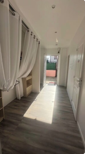 Um corredor com piso de madeira, paredes brancas e uma porta que dá para área externa.