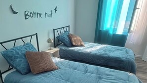 Een slaapkamer met twee bedden, een nachtkastje, een wandklok en een raam met gordijnen.