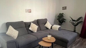Een woonkamer met een grijze modulaire bank, een ronde houten salontafel en een potplant.
