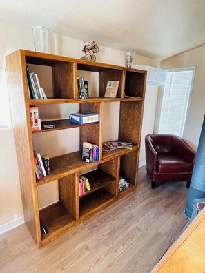 A wooden bookshelf with books and decorative items, a red leather chair, and a window with blinds.