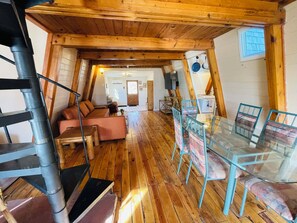 A cozy loft-style room with a wooden floor, a glass dining table, and a sofa.