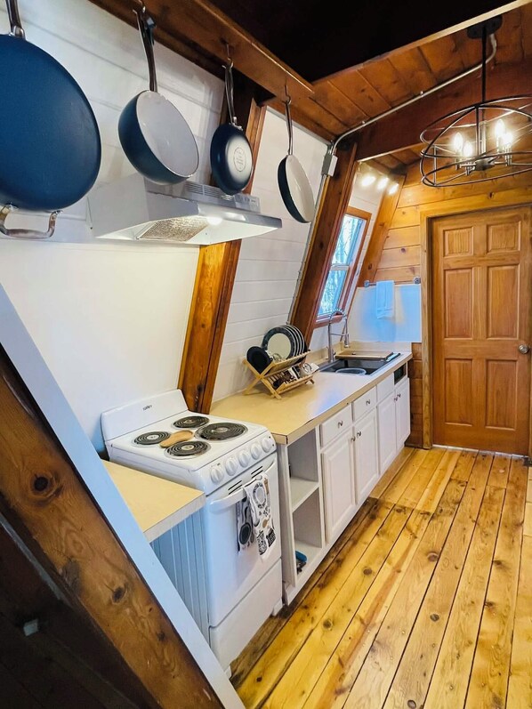A compact kitchen with a stove, white cabinets, and a wooden ceiling.