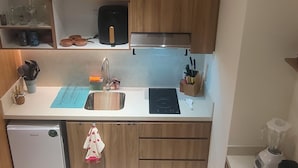 A modern kitchen with wooden cabinets, a built-in sink, a small refrigerator, and two bar stools. - Beachfront Studio ZantaMar (Cruz de Huanacaxtle)