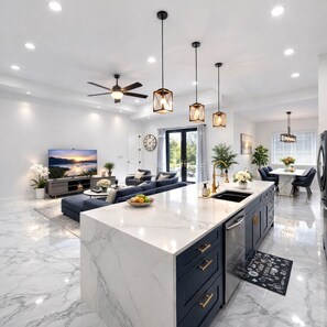 Une cuisine moderne dotée d’un îlot en marbre, de meubles de rangement aux couleurs sombres et de luminaires suspendus.