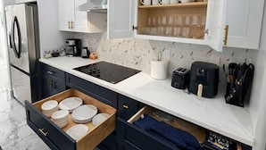 Una cocina moderna con armarios blancos, un refrigerador de acero inoxidable, un horno empotrado y una encimera de madera con cafetera y tostadora.
