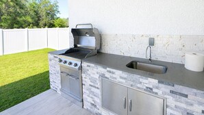 Cocina exterior con parrilla, pileta y revestimiento de piedra.
