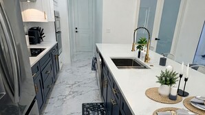 Una cocina moderna con suelo de mármol, horno empotrado y encimera blanca con fregadero y objetos decorativos.