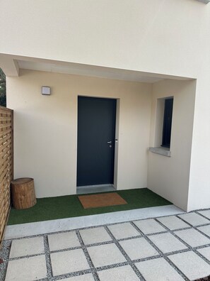 A modern building entrance with a dark door, a small window, and a wooden post. - New house 155 m² /Seaside on foot (100 m)/4 beautiful bedrooms, garden, parking (Saint-Brevin-les-Pins)