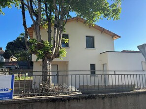 A two-story building with a balcony, a tree in front, and a sign with text. - New house 155 m² /Seaside on foot (100 m)/4 beautiful bedrooms, garden, parking (Saint-Brevin-les-Pins)
