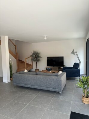 A modern living room with a grey sofa, a flat-screen TV, a coffee table, and a staircase. - New house 155 m² /Seaside on foot (100 m)/4 beautiful bedrooms, garden, parking (Saint-Brevin-les-Pins)
