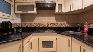 Una cocina compacta con armarios color beige, encimera negra, microondas, cafetera y una botella de detergente.
