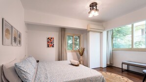 Un dormitorio con cama, una banca, una ventana y obras de arte en las paredes.