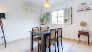 Un comedor con una mesa de madera oscura, sillas tapizadas en tonos beige, una planta en maceta y una lámpara colgante.
